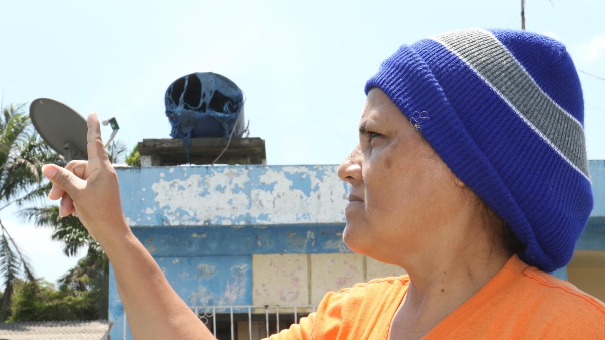 Janeth Maenza muestra su tanque de agua derretido por el calor. Su casa está a seis metros del incendio.