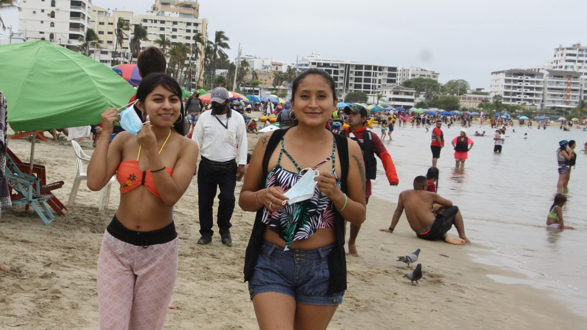 Dos visitantes se retiran las mascarillas mientras caminan por la playa de Salinas