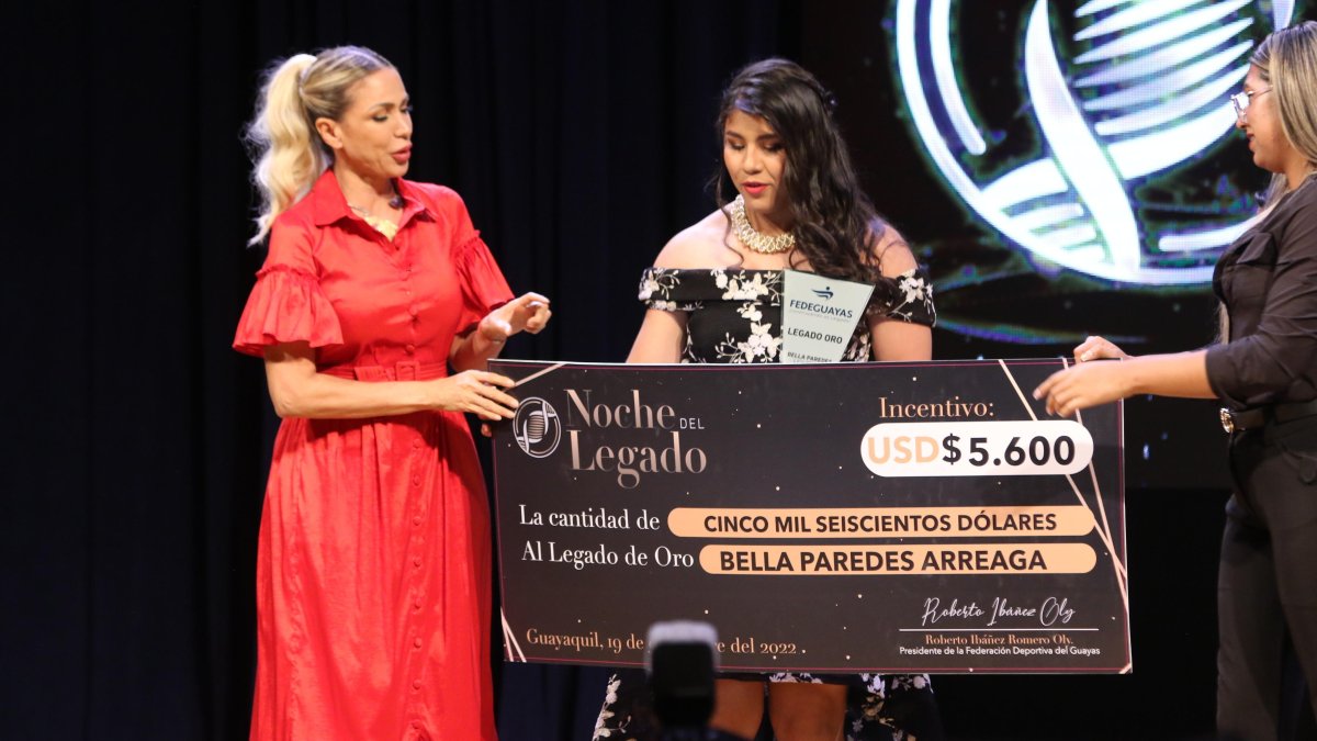 Bella Paredes recibiendo de manos de la prefecta Susana González el primero al Legado de Oro y dinero en efectivo.