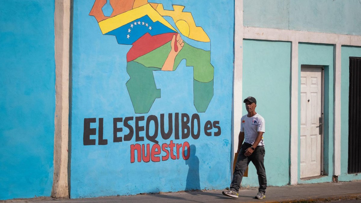 Transeúntes caminando frente a un mural con el mapa de Venezuela que dice