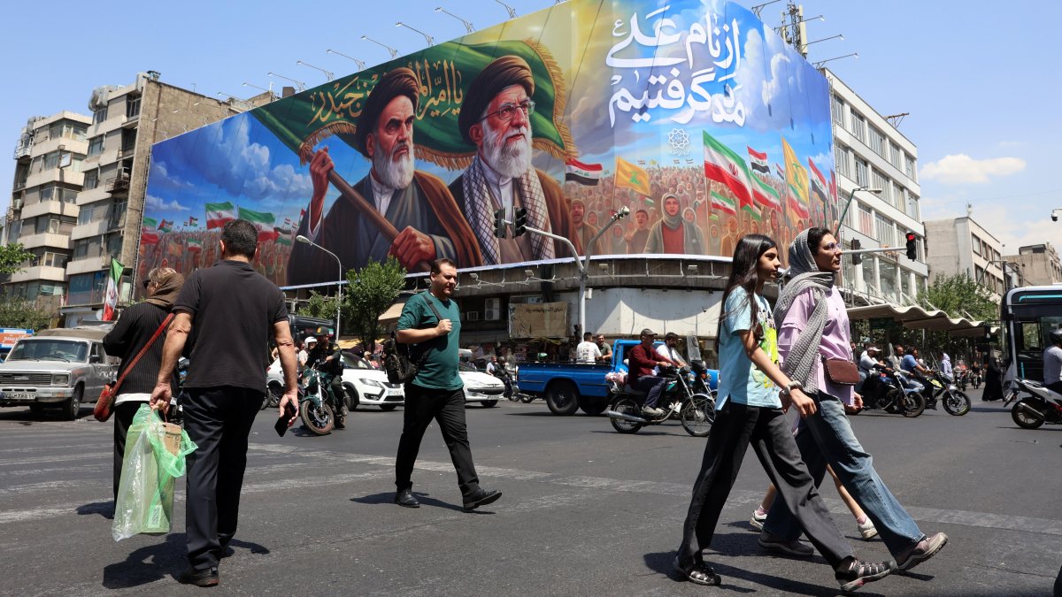 Iraníes pasan frente a una gran valla publicitaria con los difuntos líderes supremos iraníes, los ayatolás Ruhollah Jomeini y Ali Jameneí, en una calle de Teherán, Irán.