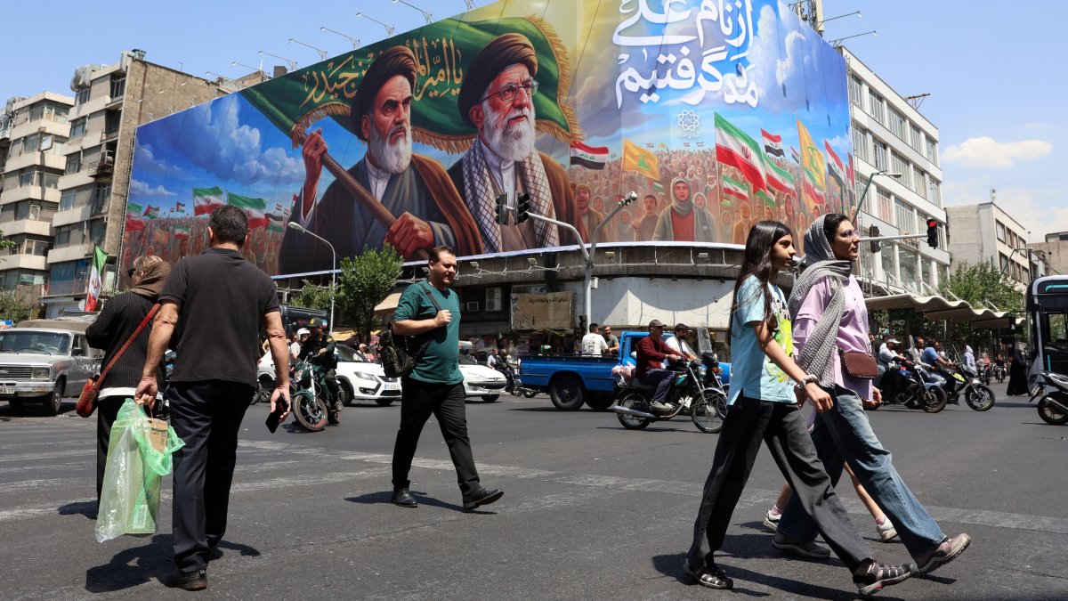 Iraníes pasan frente a una gran valla publicitaria con los difuntos líderes supremos iraníes, los ayatolás Ruhollah Jomeini y Ali Jameneí, en una calle de Teherán, Irán.