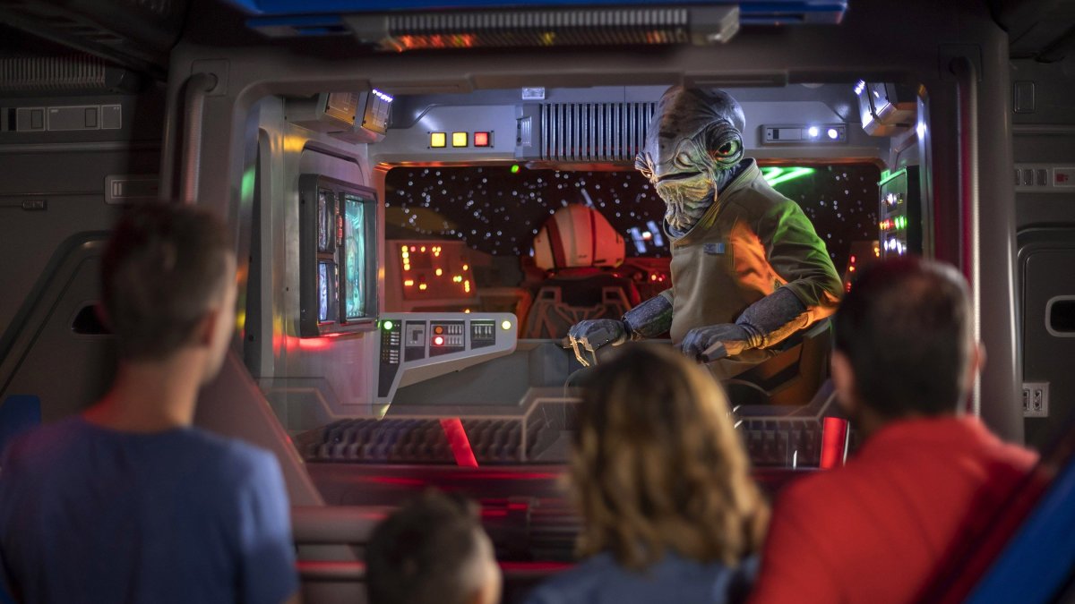 Fotografía cedida por Walt Disney World donde se muestra al teniente Bek (fondo) mientras habla con los visitantes a bordo de una nave de transporte entre sistemas, en la atracción 