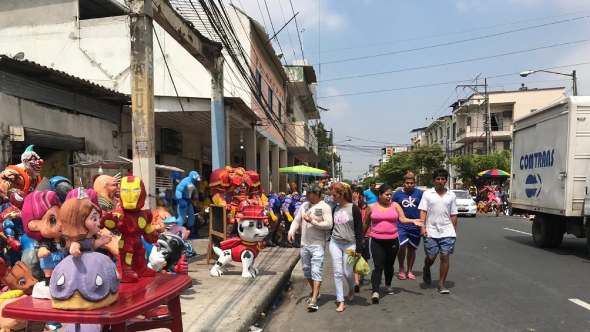 Los visitantes de la calle 6 de marzo caminan por la calzada, cerca de los carros.