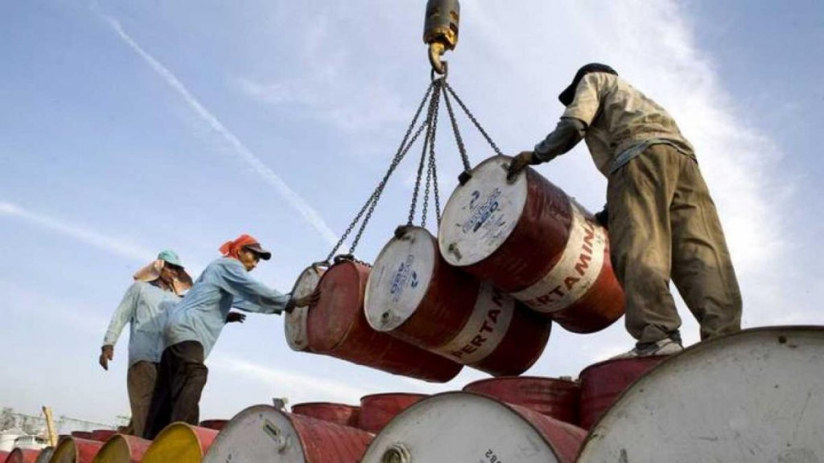 Un grupo de trabajadores mueven barriles con petróleo.