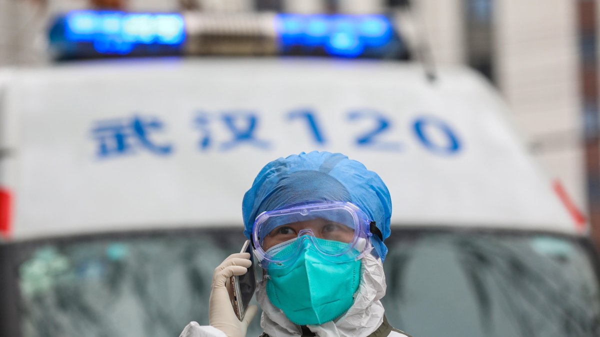 Referencial. Una enfermera totalmente protegida atiende una llamada telefónica junto a su ambulancia en Wuhan.