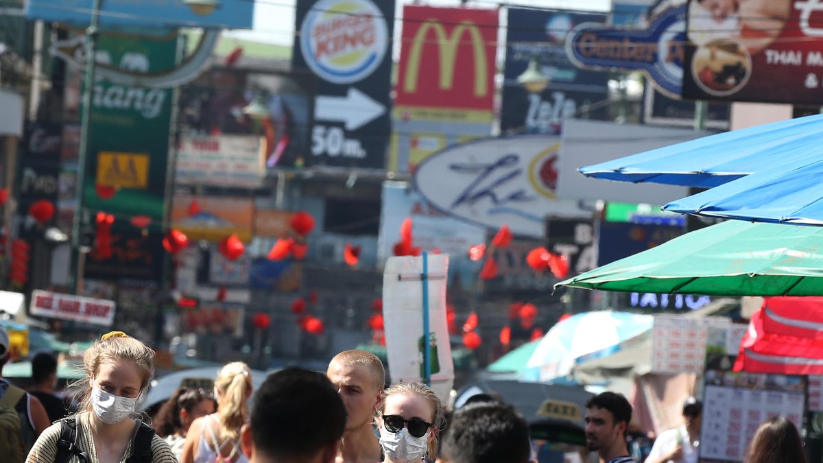 Referencial. Los turistas usan máscaras protectoras mientras caminan en la popular zona turística de Khaosan Road en Bangkok, Tailandia.