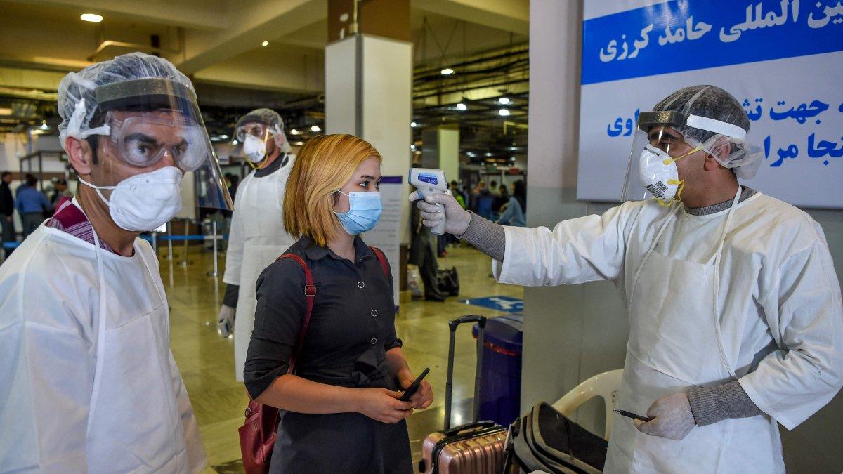 Personal de servicios de salud que usa equipo de protección verifica la temperatura corporal de un pasajero, en Kabul, por disposición de las autoridades afganas.