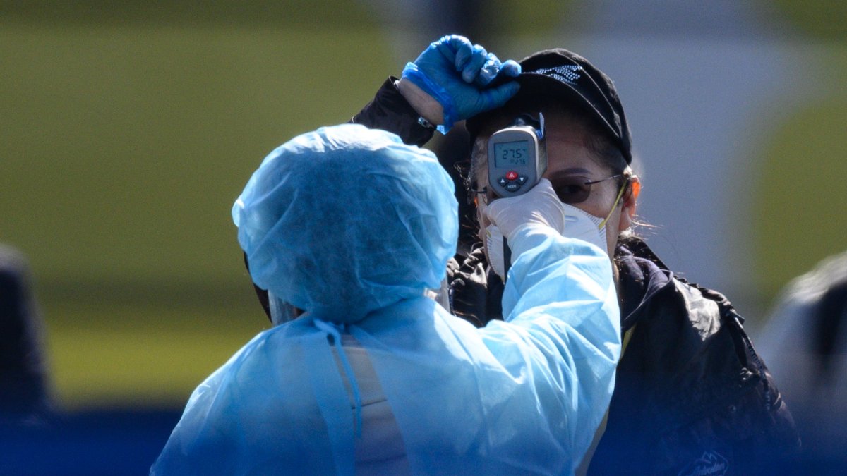Los trabajadores con ropa protectora miden la temperatura corporal a un ciudadano como medida de prevención del nuevo coronavirus COVID-19.