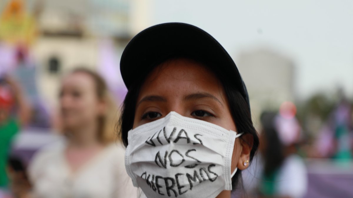 Una mujer usa un tapabocas que tiene escrito el mensaje 