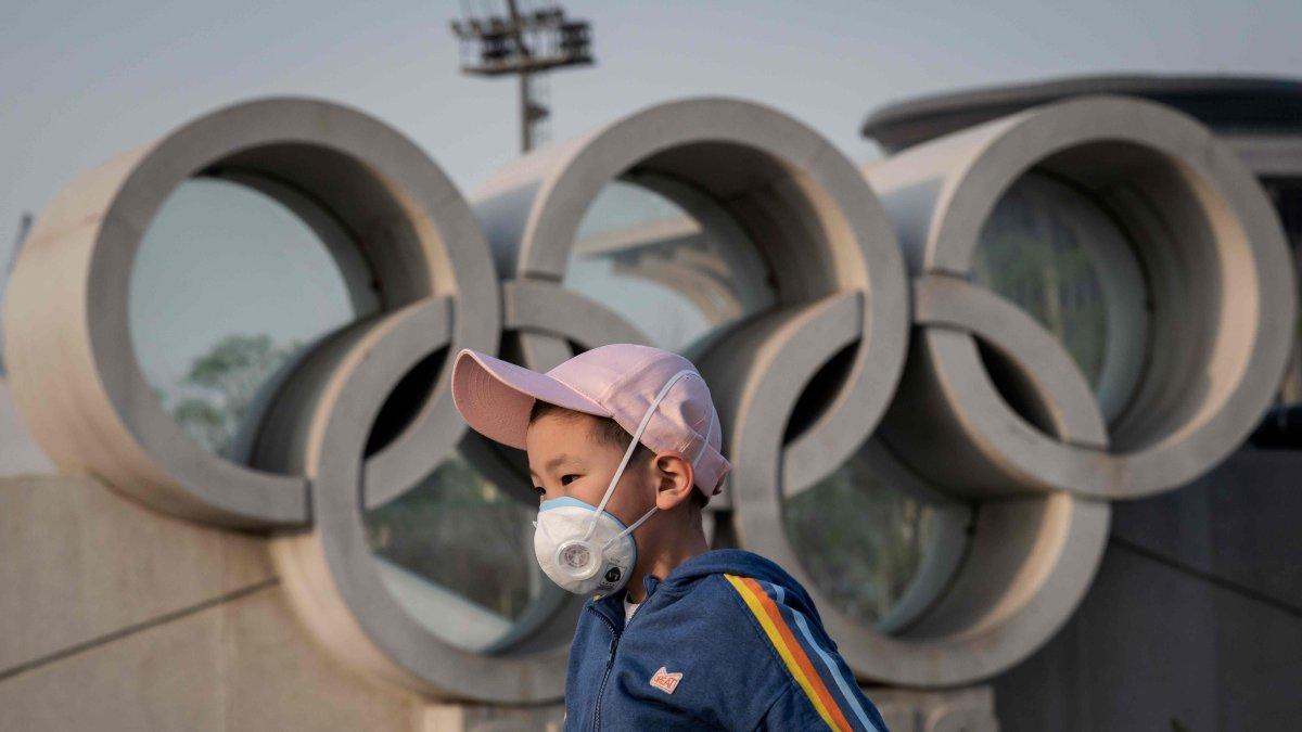 Un niño pasa con una mascarilla delante del logo de los Olímpicos.