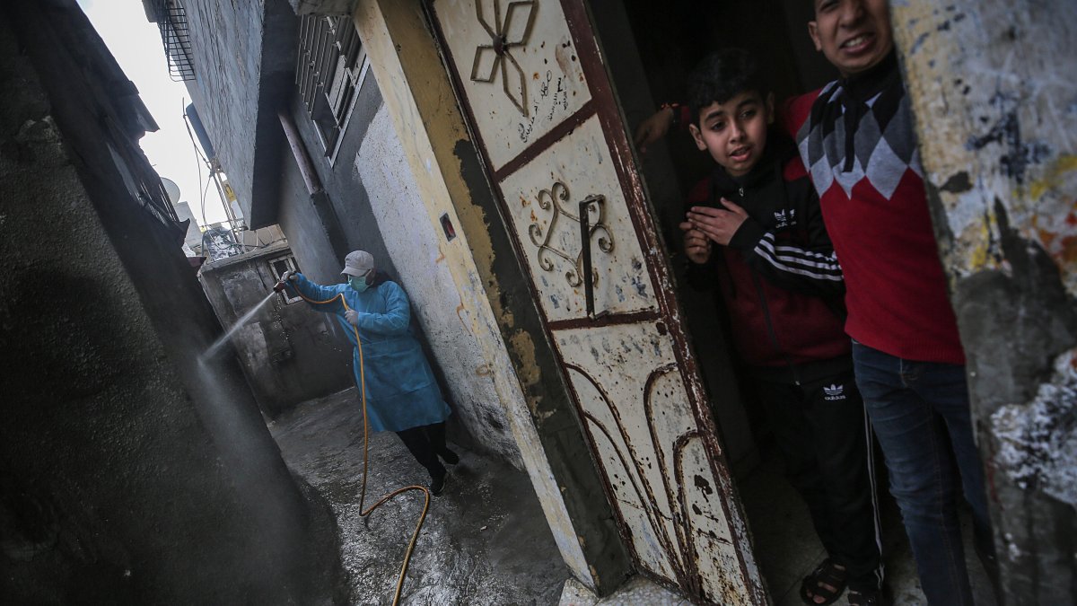 Niños palestinos observan desde la puerta de su casa como un hombre desinfecta una calle en Gaza, Palestina.