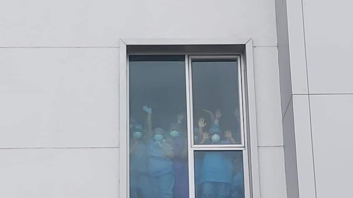 Los galenos a través de una ventana de la casa de salud, cubiertos de mascarillas y la protección requerida para su área, levantaron las manos en señal de victoria.