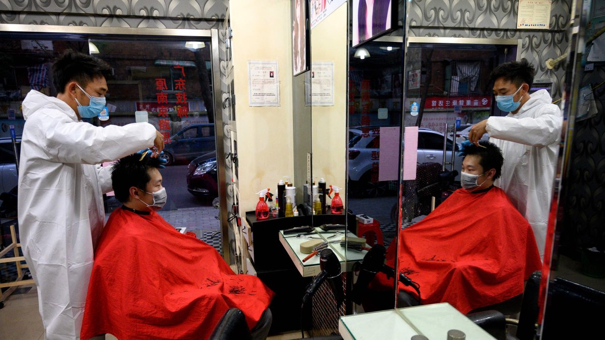 Un barbero usa un traje de bioseguridad y una mascarilla al atender a un cliente en su local en la ciudad de Wuhan.