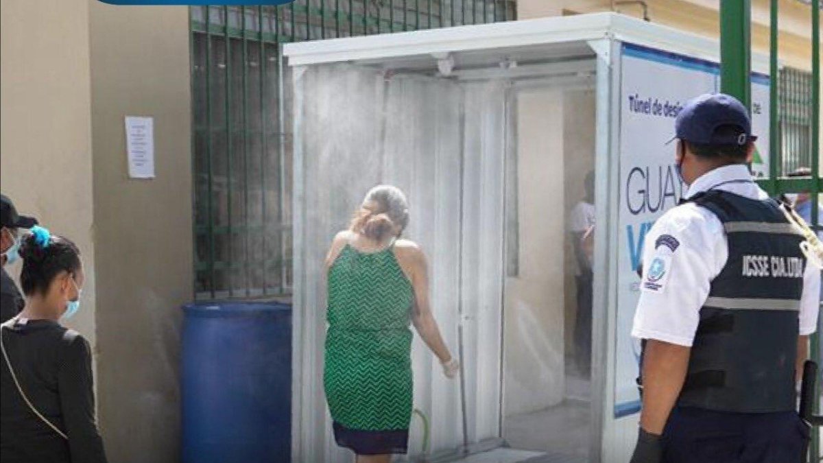 Dos personas se aprestan a pasar por el túnel de desinfección instalado en el mercado de Montebello, ubicado al norte de Guayaquil.