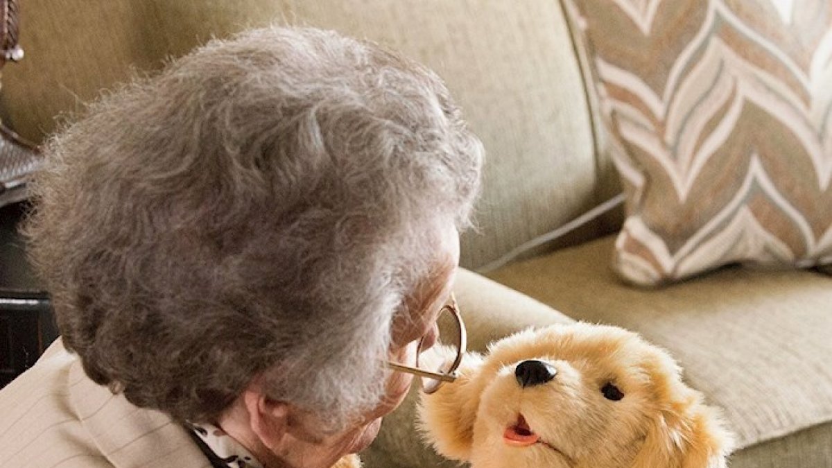 Una anciana mientras disfruta un momento de compañía con un perro robótico de la empresa Joy for All.
