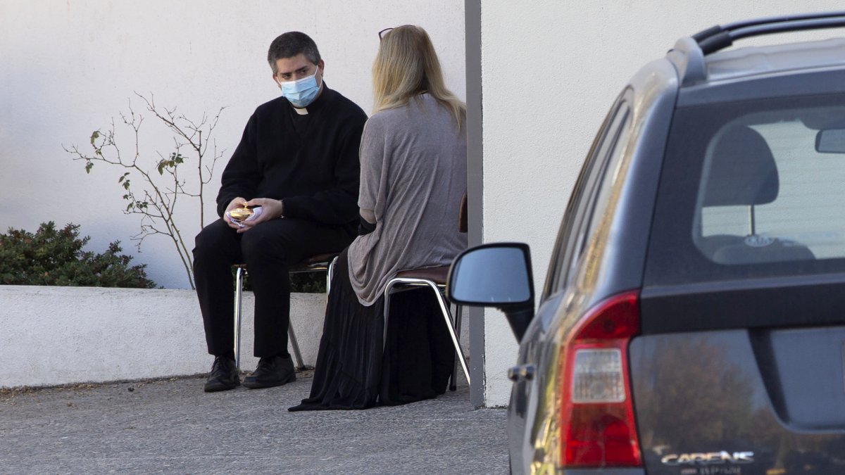 El sacerdote José, con una máscara facial, confiesa a una mujer este martes, mientras otros fieles esperan su turno en sus autos, afuera de la iglesia de San Francisco de Asís, en Santiago.