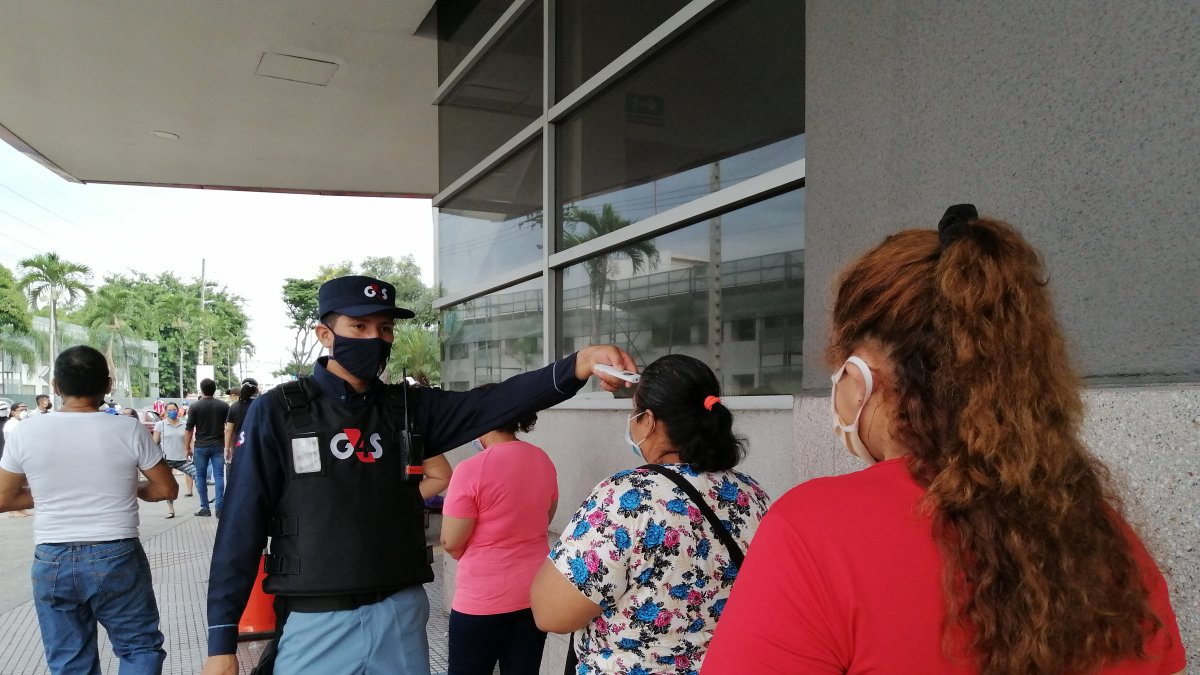 Un guardia toma la temperatura corporal a personas que quieren ingresar al Banco del Pacífico, en el Mall del Sur.