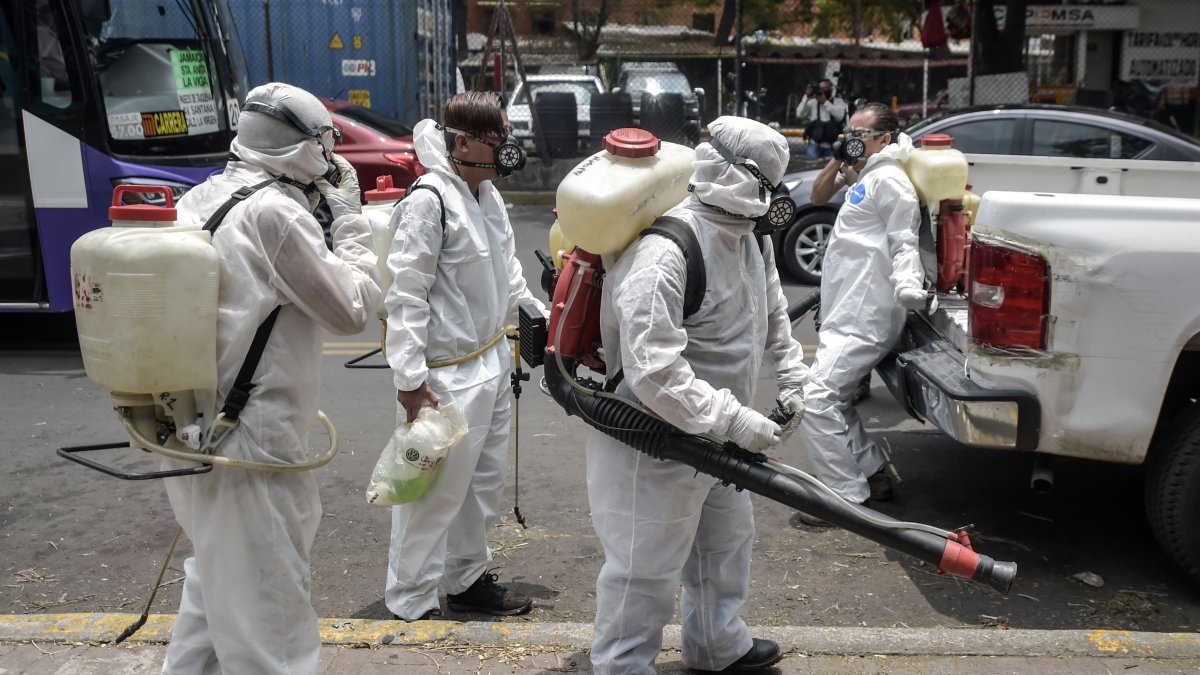 Trabajadores, protegidos con equipos de protección personal, desinfectan una calle de la Ciudad de México, en medio de la nueva pandemia de coronavirus.)