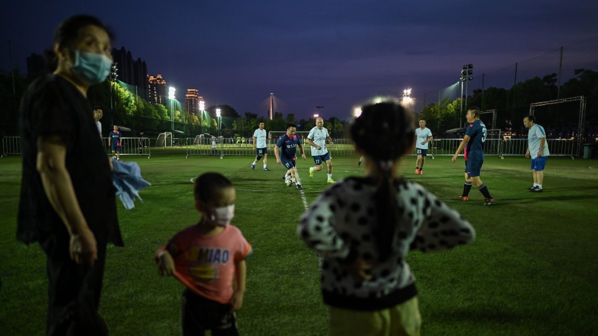 Un grupo de aficionados juegan fútbol en Wuhan, mientras son observados por personas con mascarillas.
