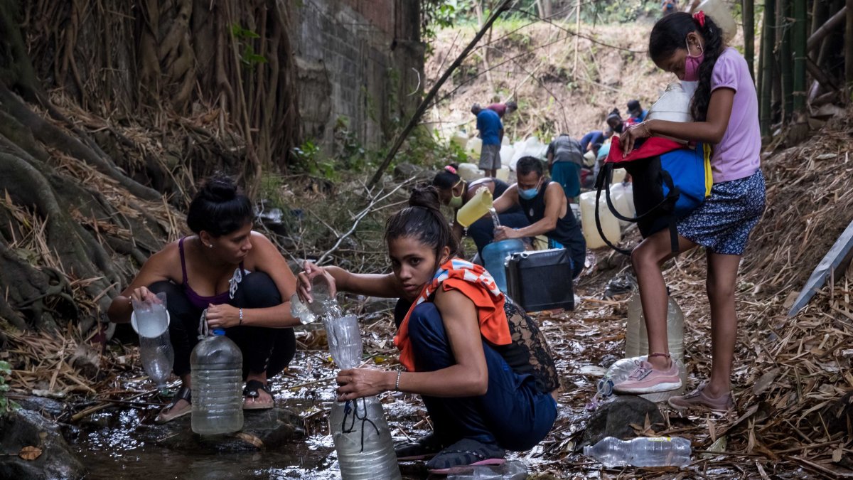 Cientos de ciudadanos recogen agua de un riachuelo.