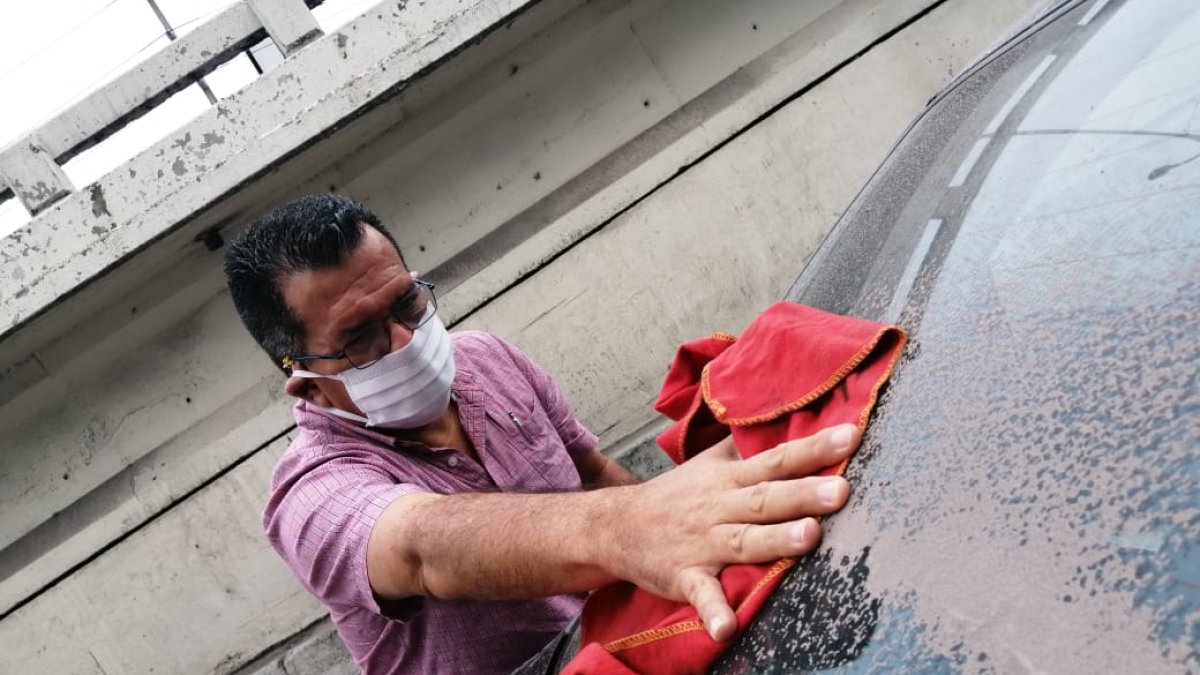 En Guayaquil, una persona retira la ceniza con un trapo; utiliza mascarilla para protegerse del COVID-19 y del polvo volcánico.