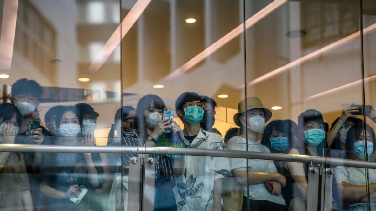 Ciudadanos con mascarilla observan a los manifestantes de una protesta contra la nueva ley de seguridad nacional para Hong Kong tras la cristalera de una tienda.
