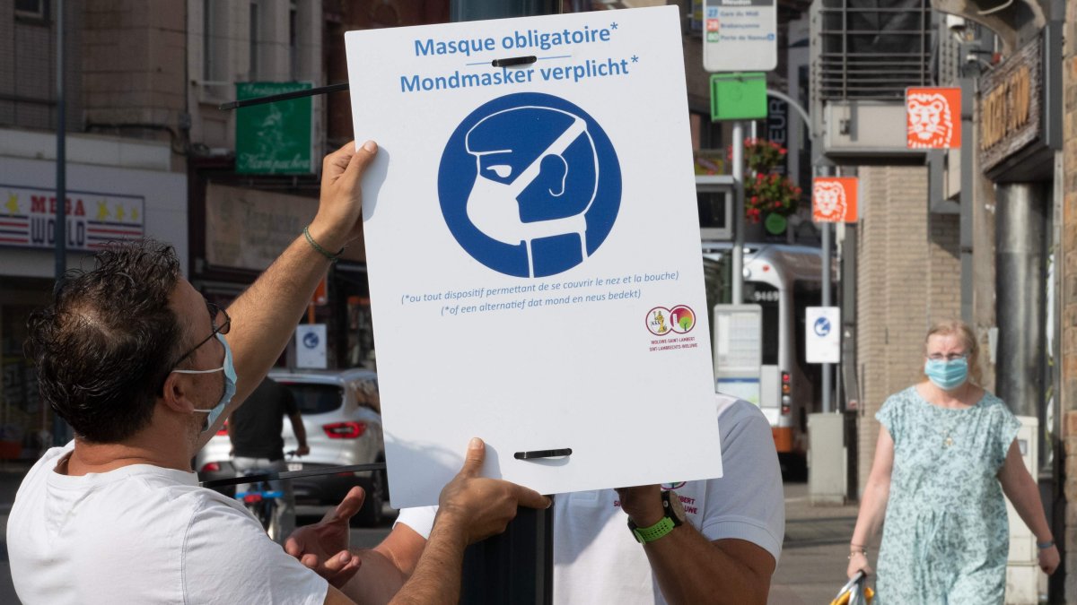 BRUSELAS. Un par de enfermeros colocan un anuncio promoviendo el uso de mascarillas en Woluwe-Saint-Lambert, aleñado a la capital de Bélgica.
