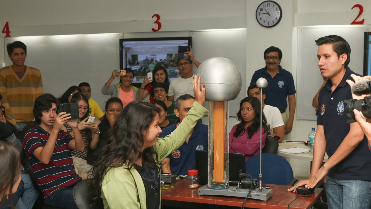 En una clase de Física, una alumna toca una esfera eléctrica. Los grupos de trabajo deben estimar el voltaje que recibió y explicarlo. Al fondo, el profesor Florencio Pinela.