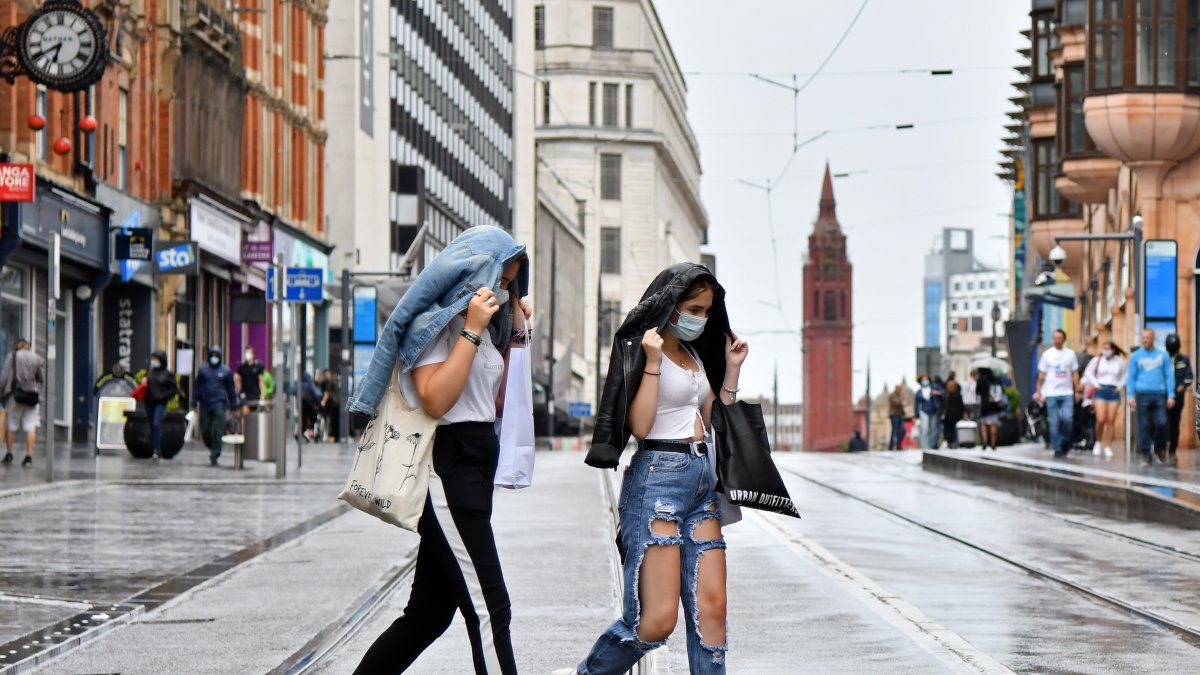 Dos mujeres con máscaras protectoras cruzan las vías del tranvía bajo la lluvia en Birmingham, en el centro de Inglaterra