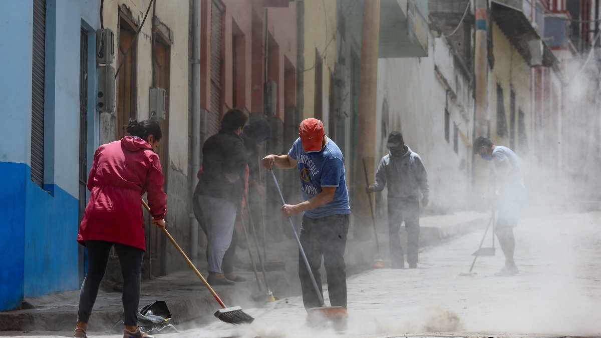 Habitantes barren la ceniza del volcán Sangay en una calle de Alausí, en la provincia de Chimborazo.