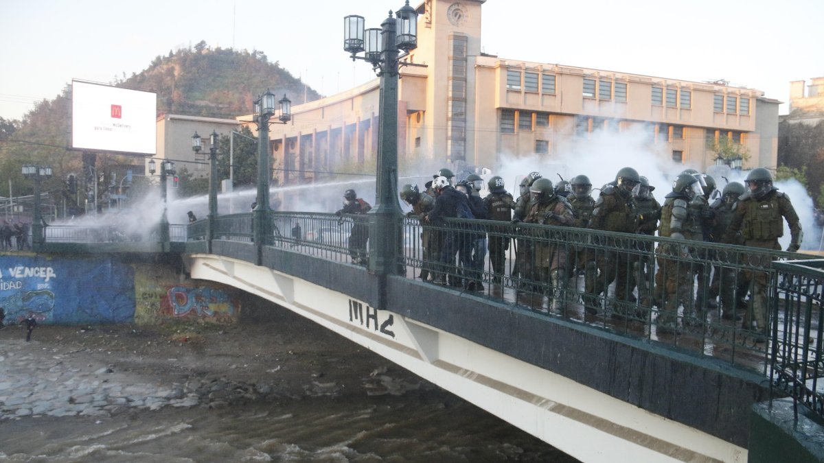 Miembros de carabineros observan a un manifestante que se encuentra inconsciente luego de caer en el río Mapocho.
