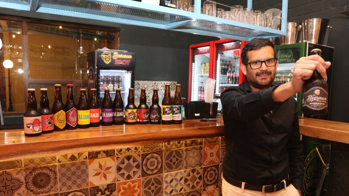 Juan Zurita, sostiene la cerveza de su marca Beerman y exhibe otras artesanales de otras marcas.