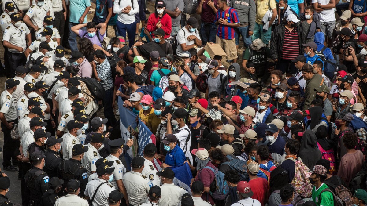 Migrantes hondureños se arrodillan para orar frente a los policías guatemaltecos, el 17 de enero de 2021.