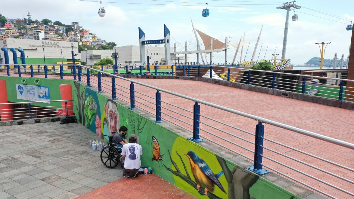 Felipe Arrobo pinta un árbol en un mural en el Malecón 2000, junto al pintor Andy Son.