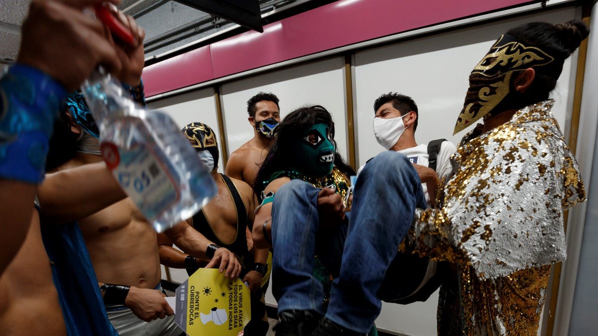 Profesionales de la lucha libre mexicana viajan concienciando del uso del tapabocas, en el metro de Ciudad de México.