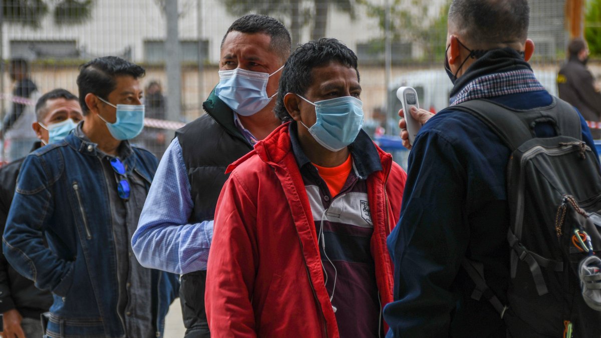 Un empleado le toma la temperatura a una ciudadana ecuatoriana residente en España vota en la segunda vuelta de las elecciones presidenciales de su país este domingo en el Palma Arena de Palma de Mallorca.