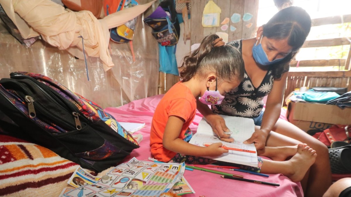 Una niña recibe clases en casa de la mano de su madre. Su hogar no cuenta con Internet.