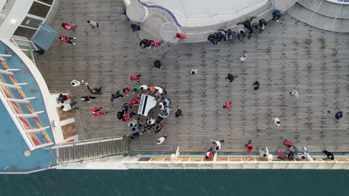 Una toma realizada con un dron muestra a un grupo de migrantes escuchando el piano en cubierta.