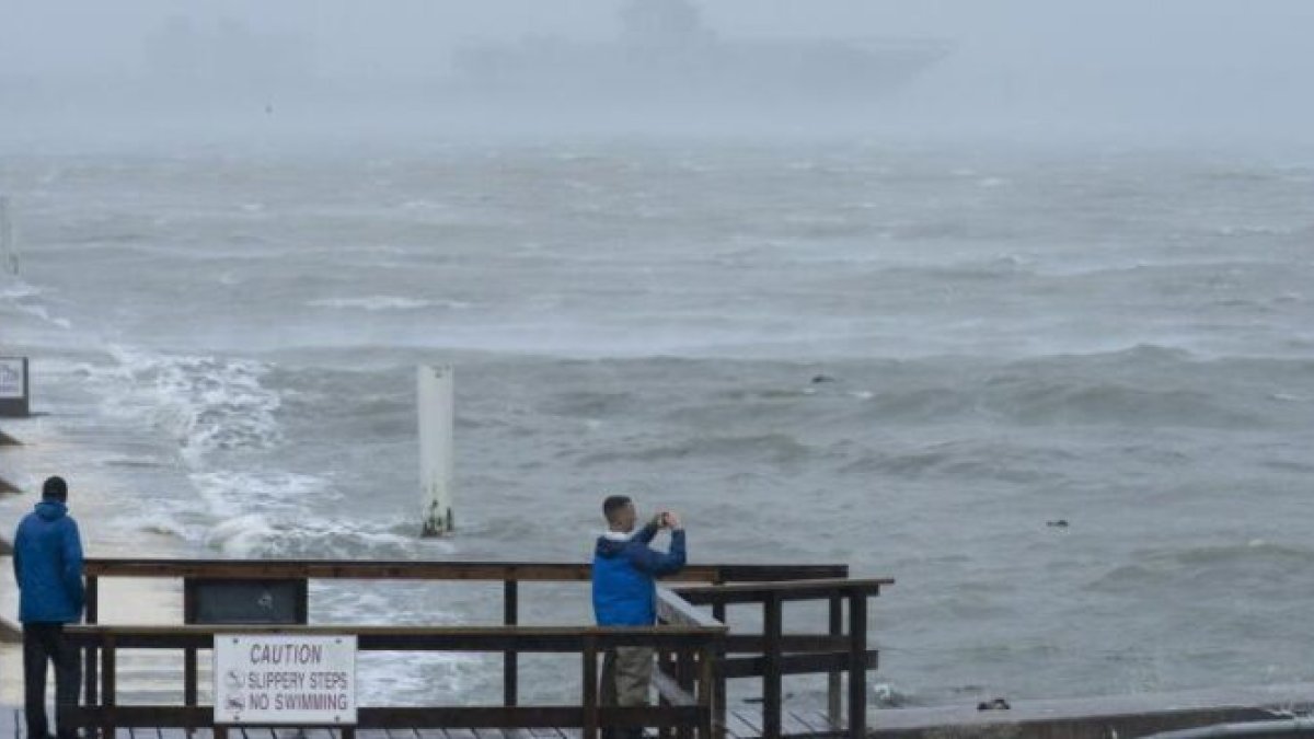 Dos hombres en un muelle de la costa de Carolina del Norte observan y uno de ellos fotografía el comportamiento del mar ante los fuertes vientos.