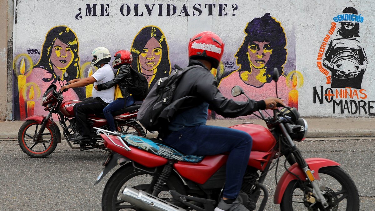 Dos motocicletas pasan frente a un mural que retrata a tres mujeres víctimas de violencia de género hoy, en Tegucigalpa (Honduras).