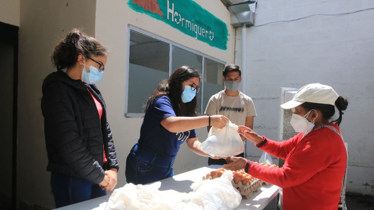 Intercambio. Alegría Parreño, Paula Herrera y Diego Yépez entregan una bolsa con alimentos a una beneficiaria de la fundación El Hormiguero.