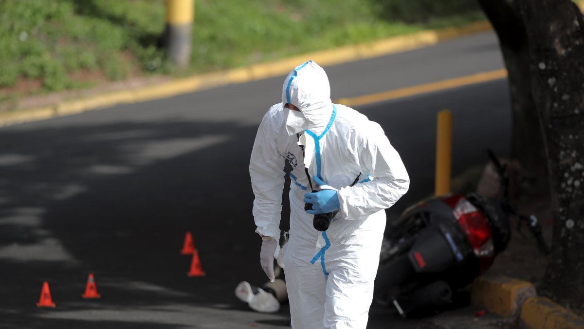 Un agente de la Dirección de Policía de Investigación inspecciona la escena donde un joven fue asesinado.