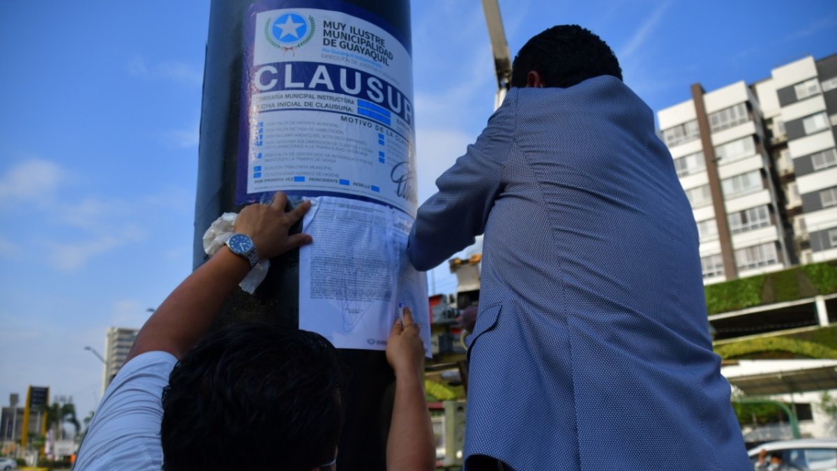 Momento en que el personal del Municipio de Guayaquil pega la sanción en el poste de una valla publicitaria.