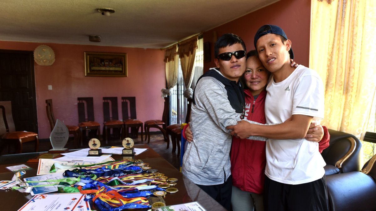 Maribel Calle (c) junto a sus dos hijos, Daniel Simbaña (i), paratleta con discapacidad visual, y Andrés Simbaña, quien además de hermano es guía del deportista en las competencias.