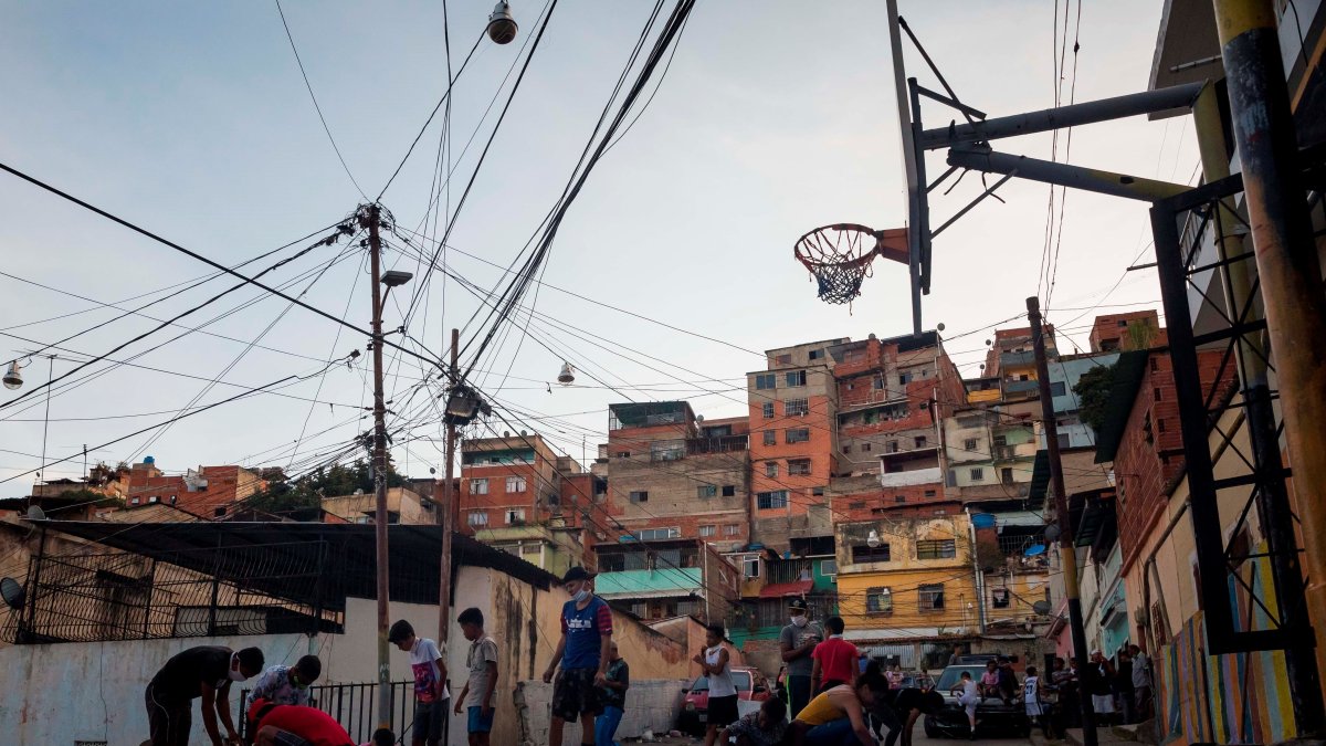 Un grupo de niños y jóvenes juega baloncesto para inaugurar una recién restaurada cancha improvisada por los vecinos del barrio.