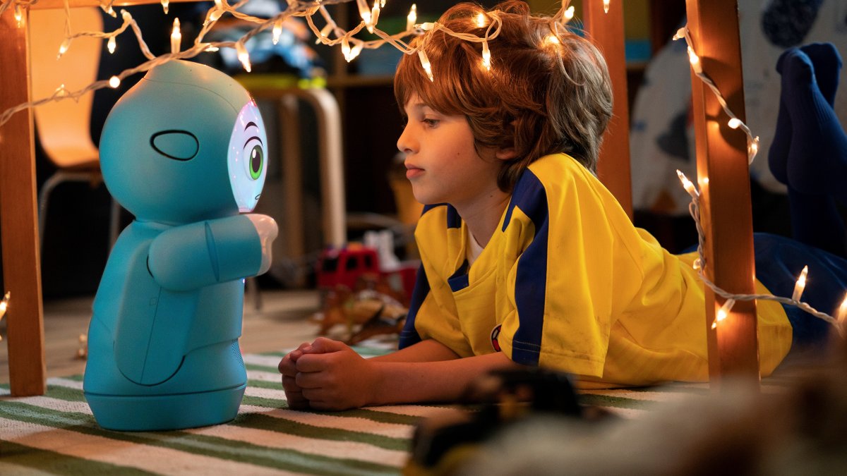 Un niño jugando con el robot Moxie en el suelo.