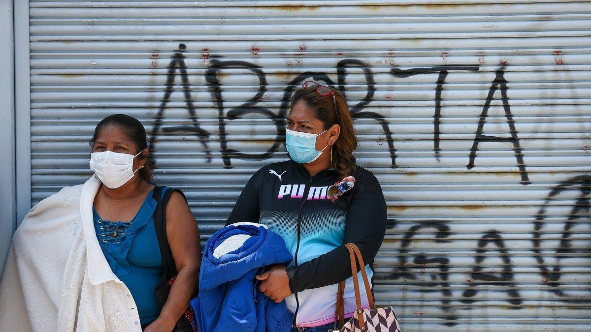 Dos mujeres permanecen frente a un rejado en el que se lee 