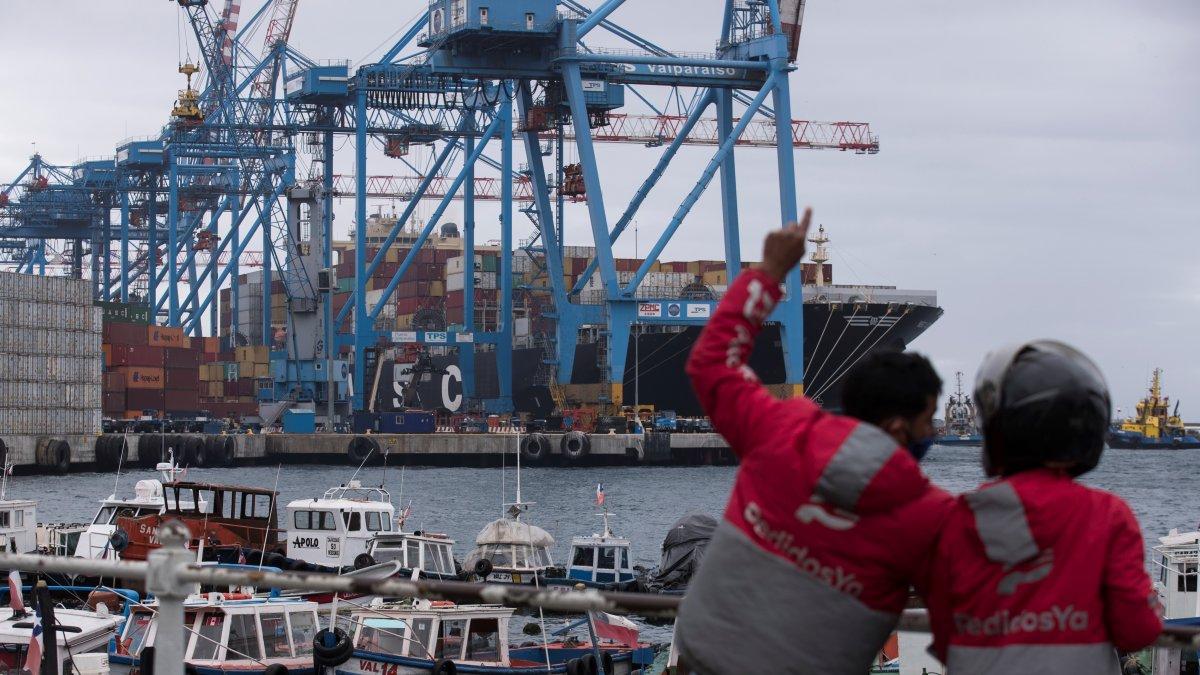 Dos repartidores de domicilios mientras observan contenedores en el puerto de Valparaíso (Chile).