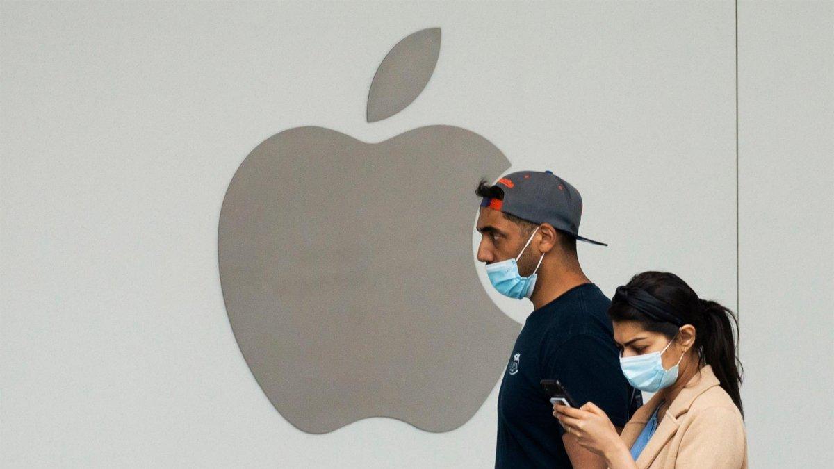 Una mujer usa un teléfono celular mientras camina frente a una tienda Apple, en una fotografía de archivo.